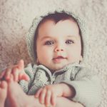 A cute baby in a knitted outfit lying on a soft carpet, smiling warmly.