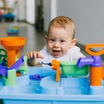 A joyful baby enjoying playtime with a colorful water toy indoors, showcasing fun and curiosity.