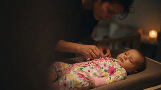 Parent changing a baby at 2 a.m. in dim nightlight, wearing a zip-front sleepsuit