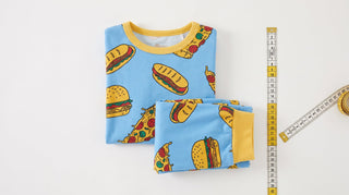 A folded pair of bamboo children's pajamas lying flat, with the yellow snug-fit safety hangtag and a tape measure beside it