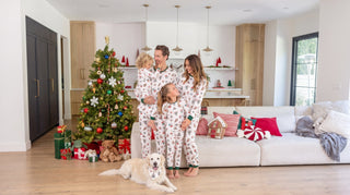Family in matching Christmas pajamas sitting by a decorated tree with their dog in a coordinating pet pajama set