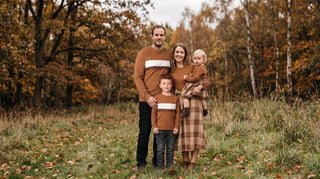 Family of four in coordinated navy, rust and cream outfits standing together outdoors in autumn light